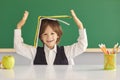 Back to school. Cheerful little boy hiding under book, playing silly game at desk in classroom. Royalty Free Stock Photo