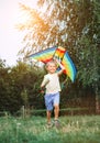 Cheerful little boy running with a multicolored kite on the city park green grass meadow. Funny childhood concept image Royalty Free Stock Photo