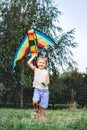 Cheerful little boy running with a multicolored kite on the city park green grass meadow. Funny childhood concept image Royalty Free Stock Photo