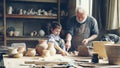 Cheerful little boy is throwing pieces of clay on work table while helping his grandfather in potter& x27;s workshop Royalty Free Stock Photo