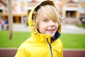 Cheerful little boy in yellow jacket is enjoying of walking on spring day. Active child playing on the street of small town.