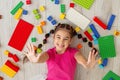 A cheerful little brunette lies on the floor, surrounded by scattered multi-colored parts of plastic constructors