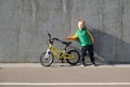 Cheerful little child boy standing near concrete wall with his yelllow bicycle on sunny day. Urban lifestyle. Active kid in the
