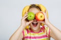 Cheerful little girl with apples, lemon and banana poses positively in studio