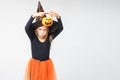 A cheerful little girl in a carnival witch costume and hat, holding a basket for treats, scares on a white background Royalty Free Stock Photo