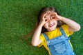 Cheerful little girl in a denim jumpsuit, lies on a green carpet, lawn Royalty Free Stock Photo