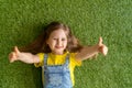 Cheerful little girl in a denim jumpsuit, lies on a green carpet, lawn Royalty Free Stock Photo