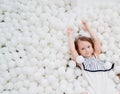 cheerful little girl in a dry pool with white balls. playground.