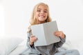 Cheerful little girl in gray pajamas holding book, looking at ca Royalty Free Stock Photo