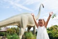 Cheerful little girl having fun in park with dinosaur replicas outdoors