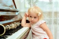 The cheerful little girl is leaning on the piano keys and pensively looks at the clarinet lying on the black piano keys Royalty Free Stock Photo