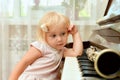 The cheerful little girl is leaning on the piano keys and pensively looks at the clarinet lying on the black piano keys Royalty Free Stock Photo