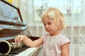 The cheerful little girl is leaning on the piano keys and pensively looks at the clarinet lying on the black piano keys Royalty Free Stock Photo