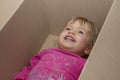 A cheerful little girl lies in a cardboard box and smiles. Concept: children`s fantasy and toys, Playhouse and family.