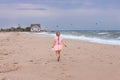 Cheerful little girl with long blonde hair in pink tulle skirt walking empty sea beach alone. Beautiful little princess Royalty Free Stock Photo