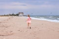 Cheerful little girl with long blonde hair in pink tulle skirt walking empty sea beach alone. Beautiful little princess Royalty Free Stock Photo