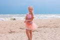 Cheerful little girl with long blonde hair in pink tulle skirt walking empty sea beach alone. Beautiful little princess Royalty Free Stock Photo