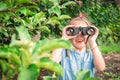 A cheerful little girl is looking through binoculars from the bushes. The child is watching the parents at a distance. The baby