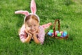 A cheerful little girl preschooler dressed in bunny ears is lying on the lawn with a basket of painted Easter eggs. Happy Easter Royalty Free Stock Photo