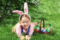 A cheerful little girl preschooler dressed in bunny ears is lying on the lawn with a basket of painted Easter eggs. Happy Easter Royalty Free Stock Photo