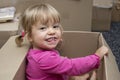 A cheerful little girl sits in a cardboard box and smiles. Concept: children`s fantasy and toys, Playhouse and family. Royalty Free Stock Photo