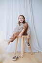 Cheerful little girl sitting on a stool, taking sandals off of her bare feet Royalty Free Stock Photo