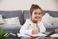 A cheerful little girl sitting at the table smiles at camera while writting something on a paper. Study at home Royalty Free Stock Photo