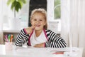 Cheerful little girl sitting at the table and smiling. On the table is a sketchbook, colored pencils, and a table lamp Royalty Free Stock Photo