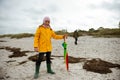 Cheerful little girl staying on beach with colorful ambrella on Baltic sea at windy rainy weather Royalty Free Stock Photo