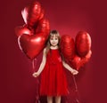Cheerful little girl in tulle skirt holding balloons red heart on red background. Celebrating brightful carnival for kids Royalty Free Stock Photo