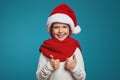 Cheerful little girl wearing christmas hat and red scarf, showing thumbs up Royalty Free Stock Photo