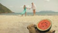 The cheerful love couple in blur, against the background of a watermelon on tropical sand beach sea. Romantic lovers two