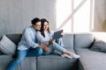 Cheerful lovely couple cuddling on sofa at home, using digital tablet for websurfing, free space Royalty Free Stock Photo