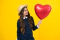 Cheerful lovely romantic teen girl hold red heart balloon, symbol of love for valentines day isolated on yellow Royalty Free Stock Photo