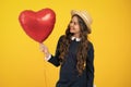 Cheerful lovely romantic teen girl hold red heart balloon, symbol of love for valentines day  on yellow Royalty Free Stock Photo