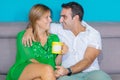 Cheerful lovely young couple sitting and drinking coffee on sofa at home