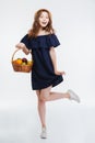 Cheerful lovely young woman in hat holding basket with fruits