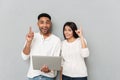 Cheerful loving couple standing over grey wall and using laptop Royalty Free Stock Photo