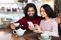 Cheerful loving indian couple have date at cafe, using phone Royalty Free Stock Photo