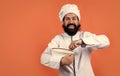 cheerful male chef in hat with beard and moustache on orange background beating meal with beater, cuisine, copy space