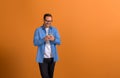 Cheerful male professional in glasses messaging over smart phone and standing on orange background Royalty Free Stock Photo