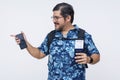 Cheerful male tourist in a tropical shirt smiling and pointing left, equipped with a cellphone, boarding pass, and passport. Royalty Free Stock Photo