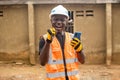 a smiling man dressed in an orange hardhat, holding up two phones and wearing Royalty Free Stock Photo