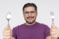 Cheerful man with glasses holding a fork and spoon with eagerness, portraying readiness for dining or mealtime