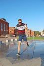 Cheerful man jumping over jets of water at fountains in hot day