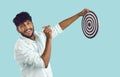 Portrait of smiling Indian guy aiming dart at dart board on light blue background. Royalty Free Stock Photo