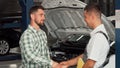 Cheerful man shaking hands with car mechanic at service shop Royalty Free Stock Photo
