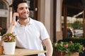 Cheerful man sitting in cafe outdoors while talking by mobile phone. Royalty Free Stock Photo