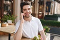 Cheerful man sitting in cafe outdoors while talking by mobile phone. Royalty Free Stock Photo