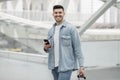 Cheerful Man Using Mobile Phone Standing With Suitcase In Airport Royalty Free Stock Photo